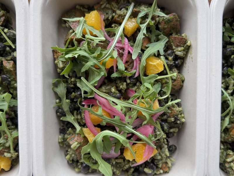 Black bean and sweet potato bowl topped with arugula, orange and pickled onion
