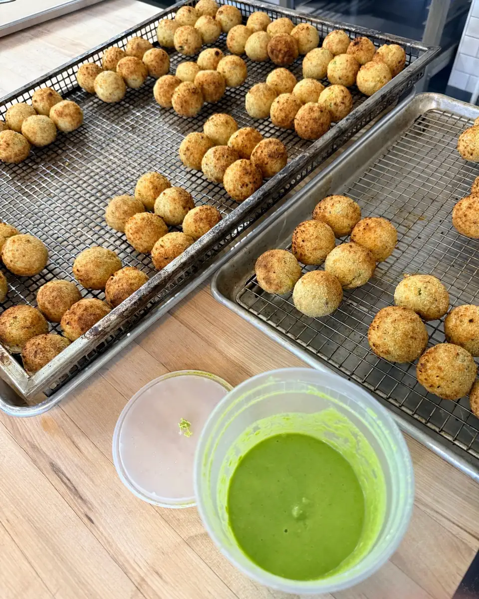 Fresh arancini cooling on racks beside pea purée